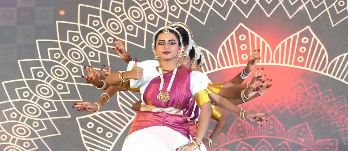 Classical dancers in a many-armed pose in front of a mandala backdrop